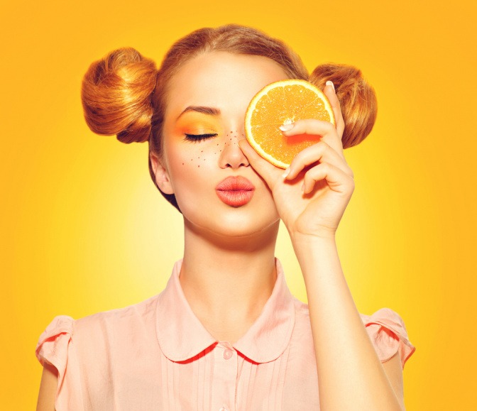 Eine Frau hält sich eine Orangenhälfte vor das Gesicht