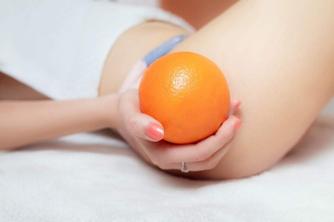 Eine Orange neben einem Oberschenkel als Zeichen für Orangenhaut