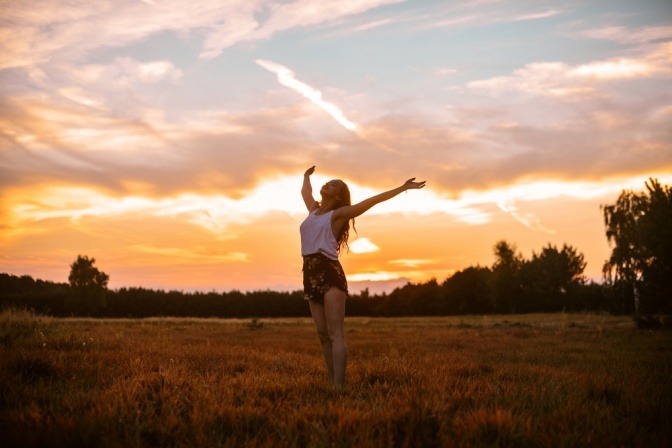 Eine glückliche, befreit und zufrieden wirkende Frau auf einem Feld bei Sonnenuntergang.