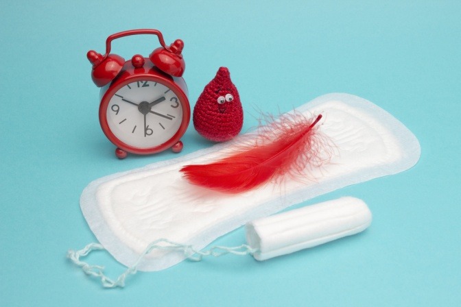 Damenbinde mit roter Feder und Wecker als Symbol für die Periode