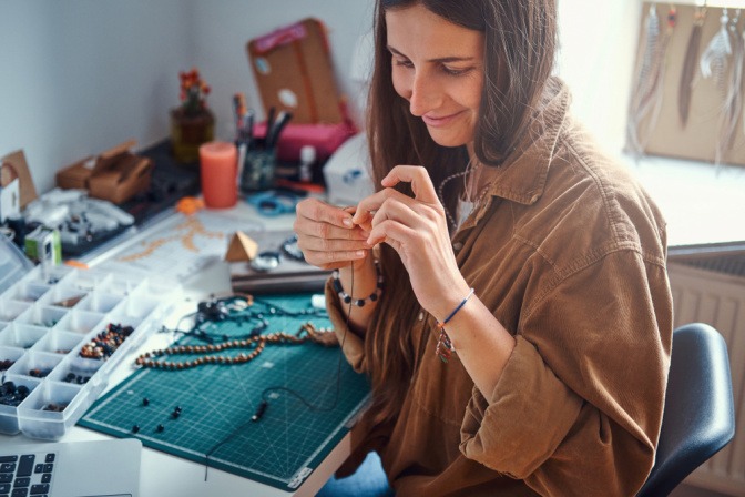 Frau beim Auffädeln von Perlen für ihre DIY-Halskette.