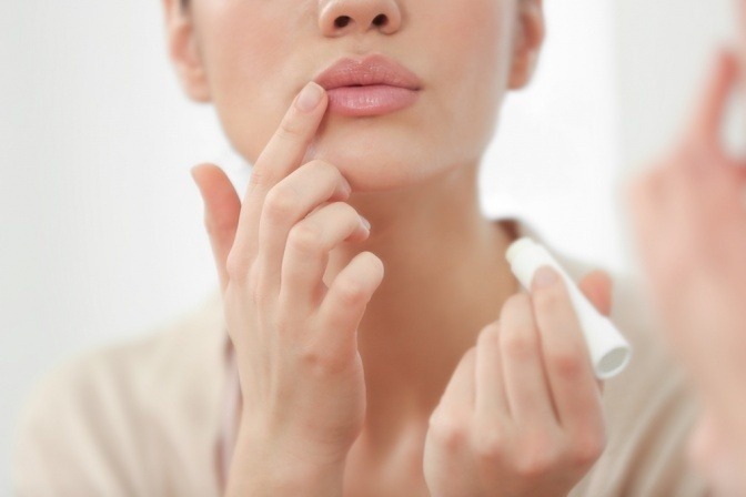 Frau trägt Pflegestift auf Lippe gegen Herpes auf