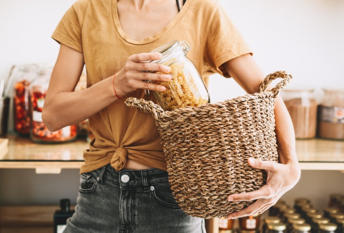 Frau mit einem Glasbehälter, gefüllt mit Nudeln und einem Bastkorb in der Hand.