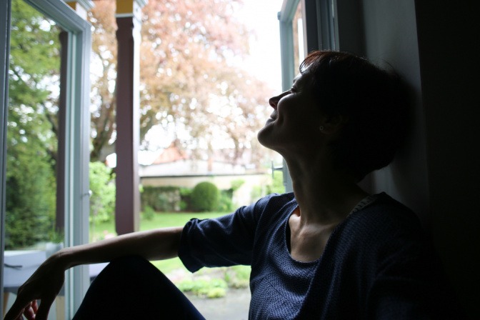 Frau sitzt am Morgen bei geöffnetem Fenster
