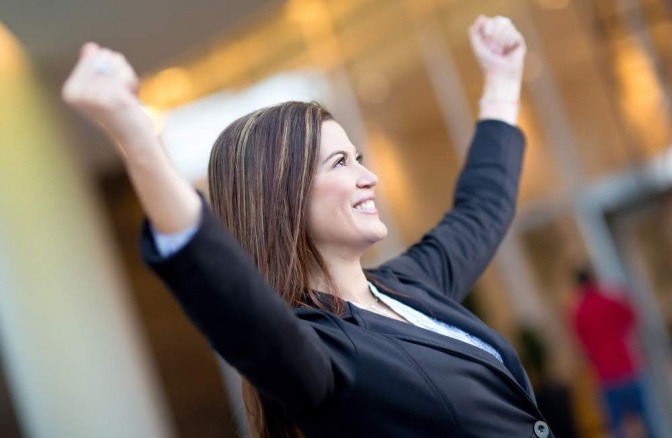Eine Frau in einem Businessoutfit reckt triumphierend die Arme in die Luft und wirkt glücklich. Es scheint, als wüsste sie genau, wie sie ihr Potential entwickeln und nutzen kann.