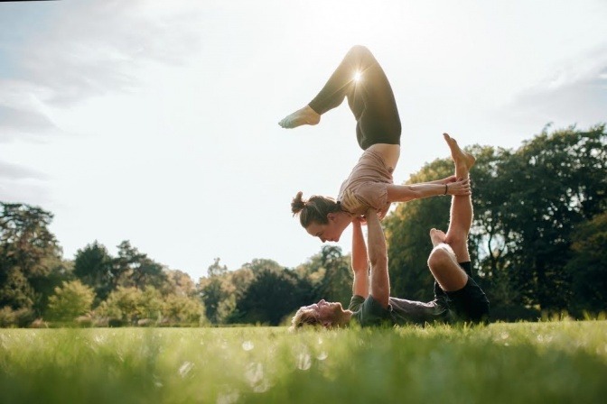 Ein Paar macht bei Sonnenaufgang gemeinsam Power-Yoga auf einer Wiese in einem Park. 