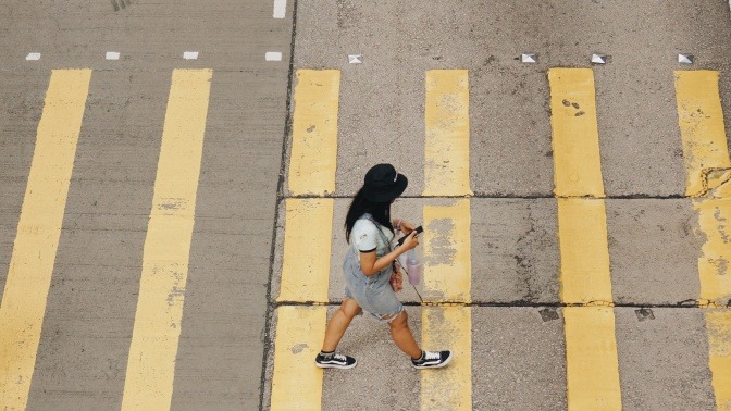 Eine Frau läuft über einen Zebrastreifen und starrt dabei auf ihr Smartphone.