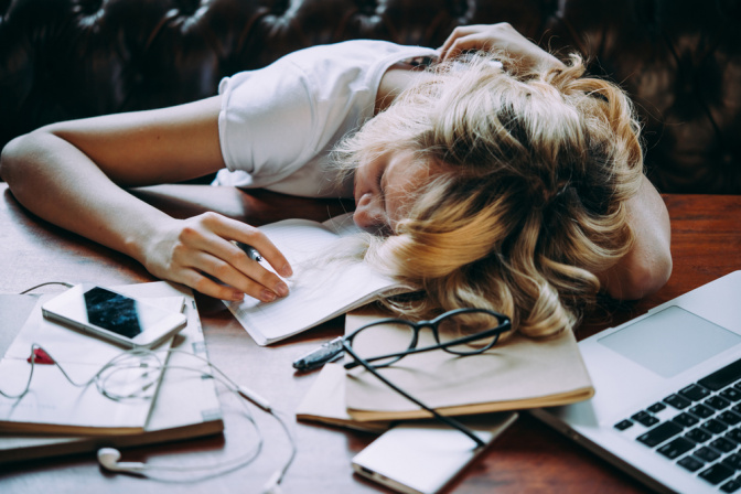 Ein junges Mädchen schläft auf einem unordentlichen Schreibtisch