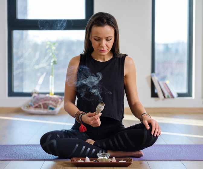 Frau beim Yoga hält ein glühendes Räucherbüschel aus Salbei