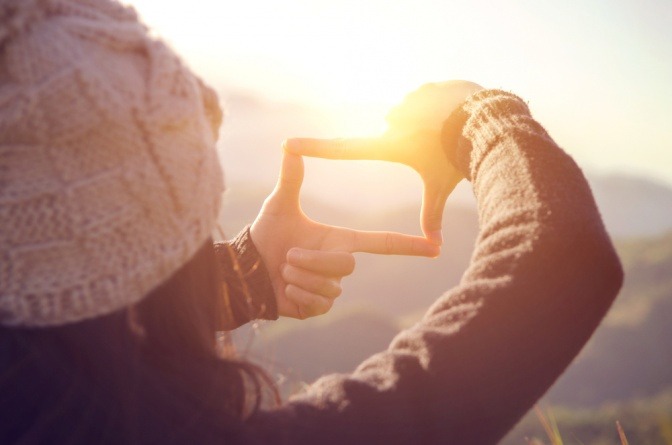 Hände einer Frau machen Rahmen um Sonnenaufgang auf Berg.