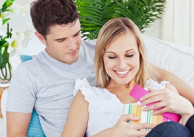 Ein Paar sitzt auf einem Sofa, die Frau erhält gerade ein Geschenk vom Partner.