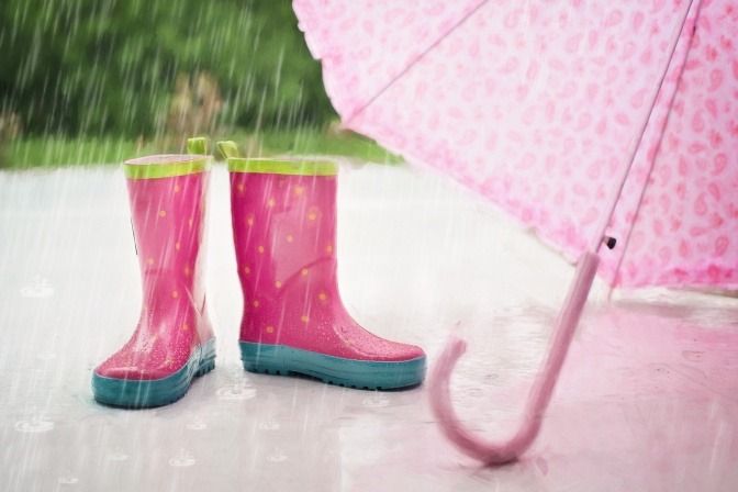 Gummistiefel und Regenschirm stehen im Regen