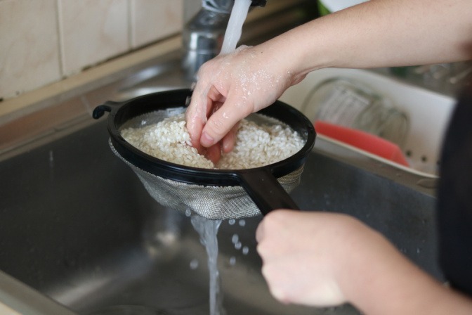 Eine Person wäscht Reis in einem Sieb unter fließendem Wasser.