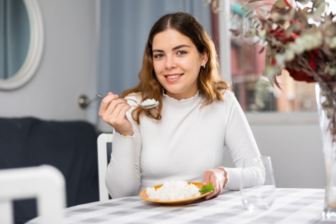 Reis waschen - junge Frau sitzt mit einer Schüssel voll weißem Reis am Tisch.