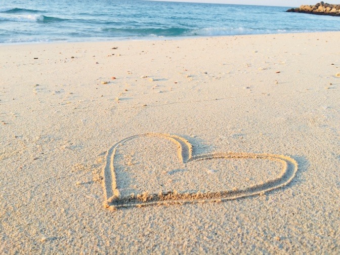 Ein Strand, an dem jemand ein großes Herz in den Sand gemalt hat.