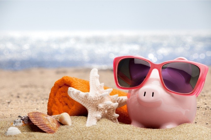 Ein Sparschwein ist auf einem Strand und Utensilien zum Reisen