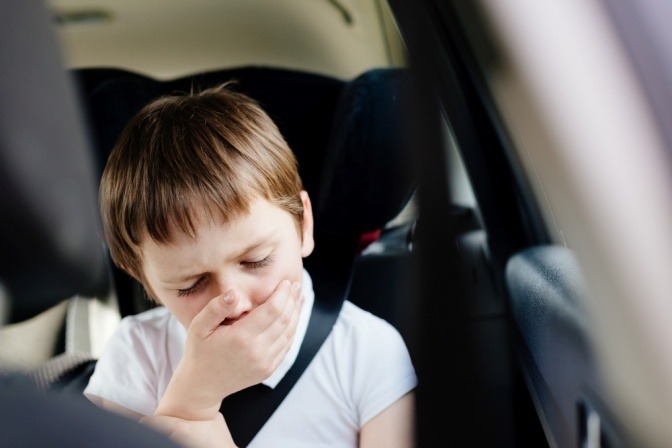 Junge hält sich bei Autofahrt die Hand vor den Mund.