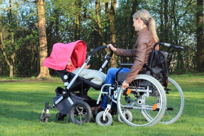 Eine Frau im Rollstuhl schiebt ihren Kinderwagen vor sich her.