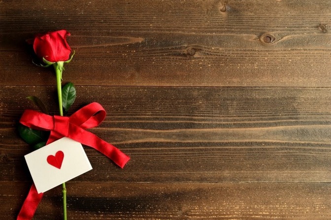 Wer einen romantischen Abend gestalten möchte, ist mit Rosen schonmal ganz gut beraten. In diesem Bild liegt die Blume der Liebe zusammen mit einem Umschlag, der mit einem Herz verziert ist, auf einem Holztisch.