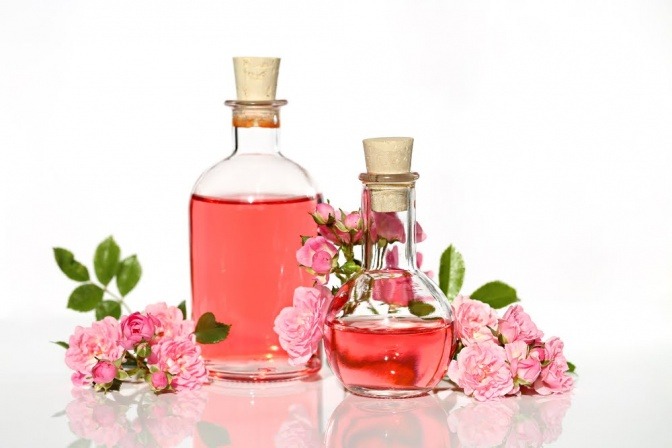 Neben Blüten von Rosen sind Fläschchen mit Rosenwasser