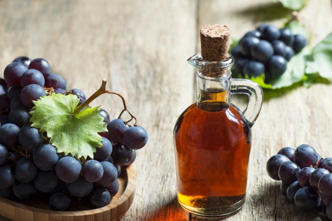 Flasche mit Rotweinessig, daneben Trauben