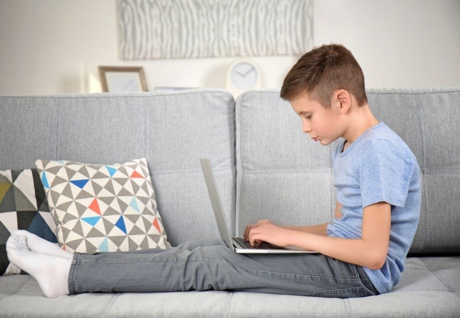 Kind mit Laptop auf dem Sofa