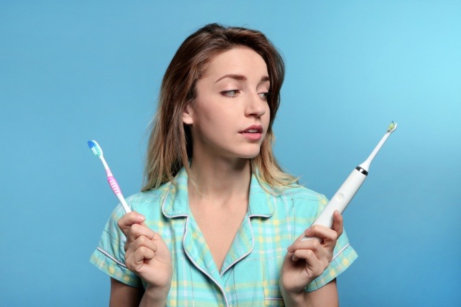 Frau mit Handzahnbürste und elektrischer Zahnbürste