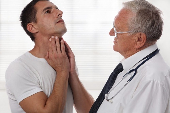 Ein Mann greift neben einem Arzt auf seine Schilddrüse