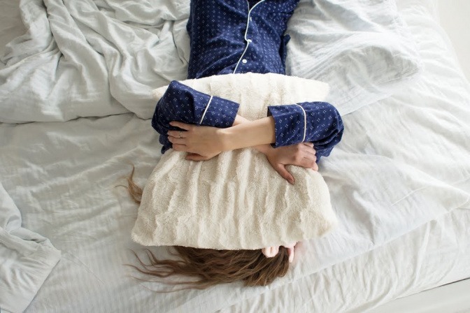 Eine Frau hält sich im Bett ein Kissen über den Kopf