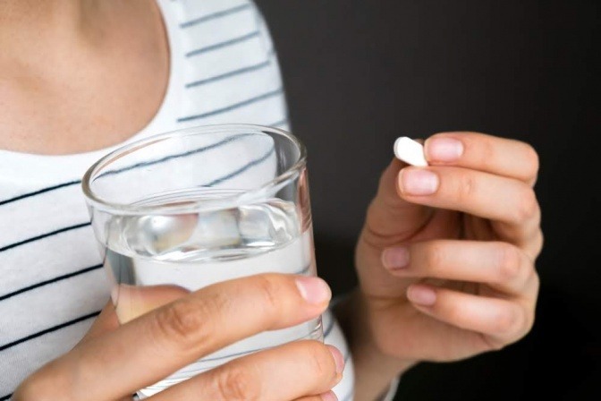 Eine Frau hält in der einen Hand ein Glas Wasser und in der anderen Hand eine Schlaftablette.