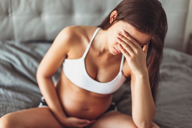 Eine schwangere Frau sitzt erschöpft im Bett