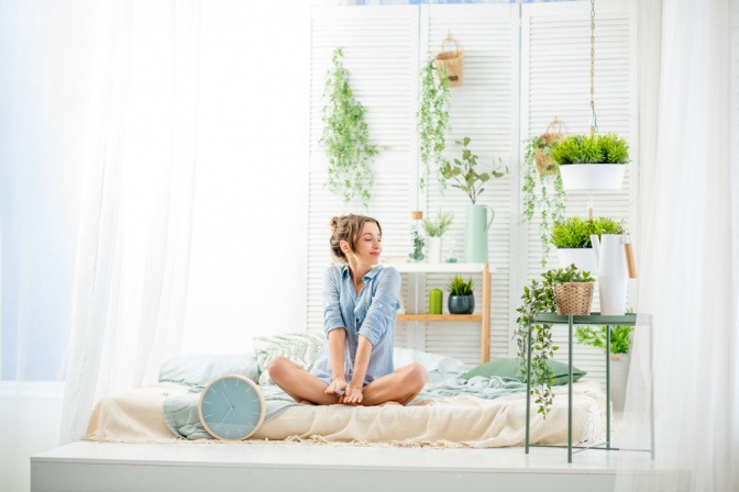 Schlafzimmer Pflanzen - glückliche Frau in einem lichtdurchfluteten Schlafzimmer mit vielen Pflanzen.