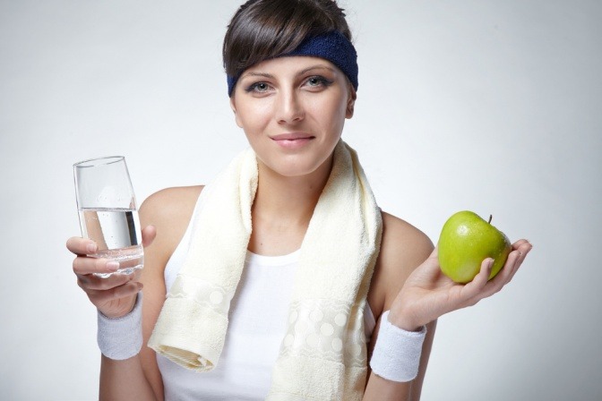 Eine gesunde, junge und sportliche Frau hält einen Apfel und ein Glas Wasser hoch.