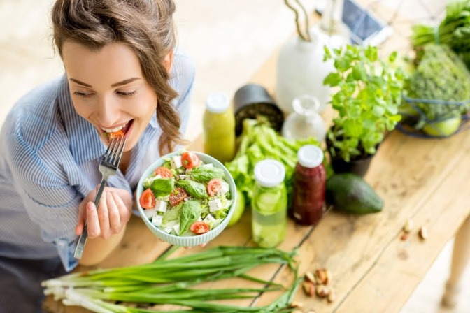 Eine Frau sitzt am Küchentisch und isst Salat aus einer Schüssel.