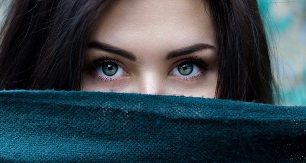 Eine Frau mit schönen Augen blickt hinter einen Stoff hervor