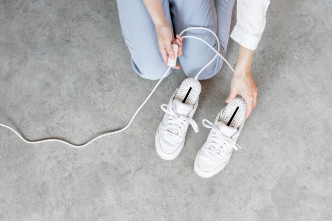 Frau benutzt elektrische Schuhtrockner zum Trocknen der Schuhe