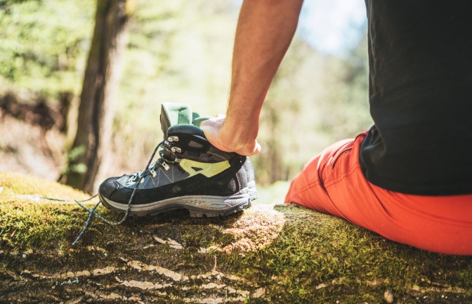 Mann legt bei einer Wanderung seine nassen Schuhe auf einen Baumstamm zum Trocknen.