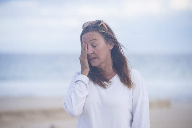 Eine Frau macht einen Spaziergang am Strand. Sie wirkt nachdenklich und scheint gerade eine Erkenntnis zu haben, vielleicht bezüglich ihrer Schuldgefühle.