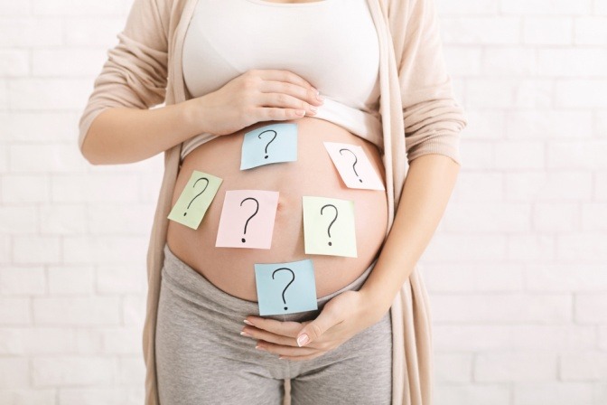 Schwangere Frau mit Babybauch mit Fragezeichen