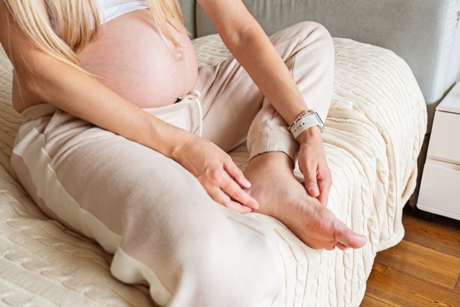 Eine schwangere Frau betastet ihre geschwollenen Knöchel