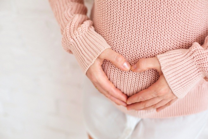 Bauch einer Schwangeren die ein Herz mit ihren Händen darüber formt