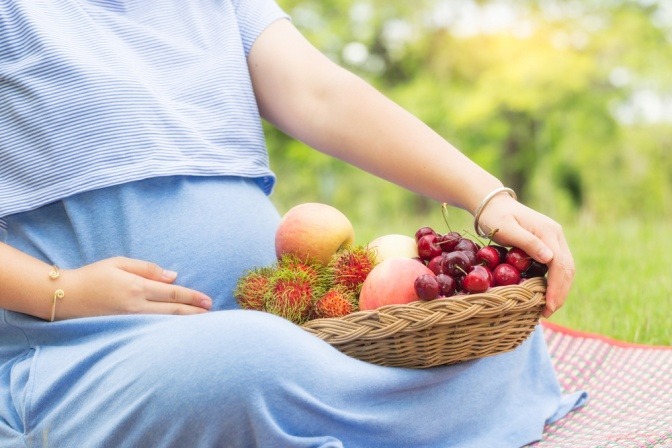 Ausschnitt von schwangerer Frau mit einer Schale Früchten im Schoß
