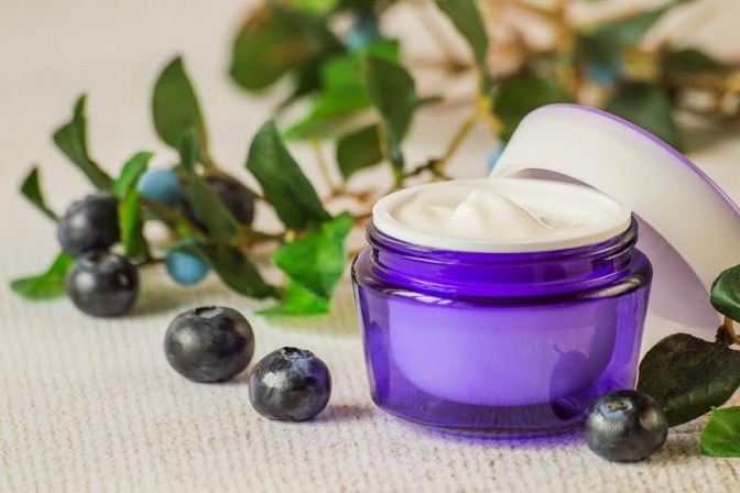 Neben einem Creme-Tiegel befinden sich schwarze Beeren