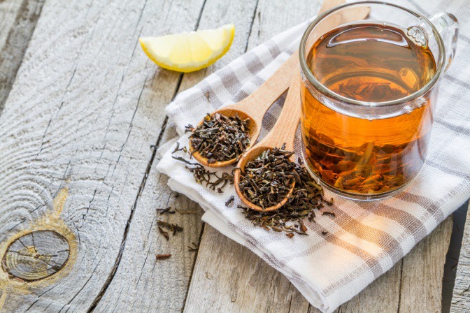 Neben einer Tasse schwarzem Tee liegen Teeblätter