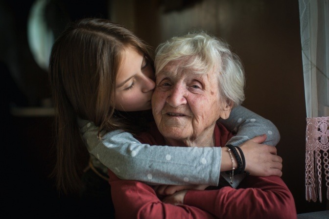 Eine junge Frau umarmt eine ältere Dame, die dies sichtlich genießt.