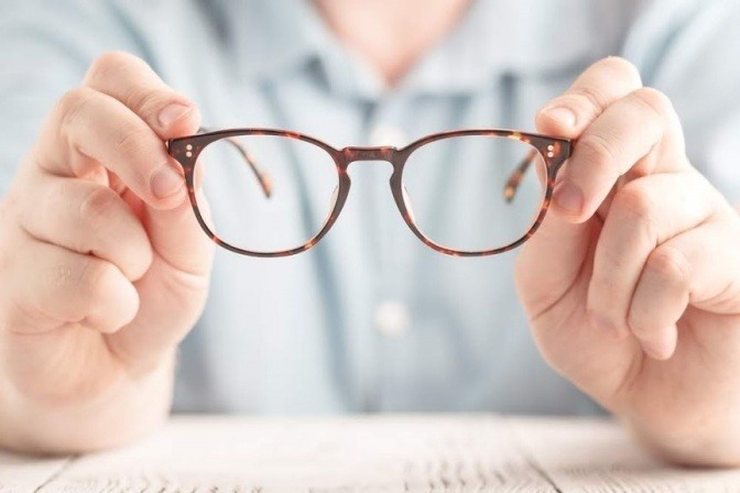 Ein Mann (vielleicht mit Sehstörungen durch Stress) hält eine Brille in der Hand