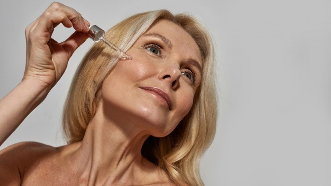 Frau träufelt mit Pipette Serum auf ihre Haut