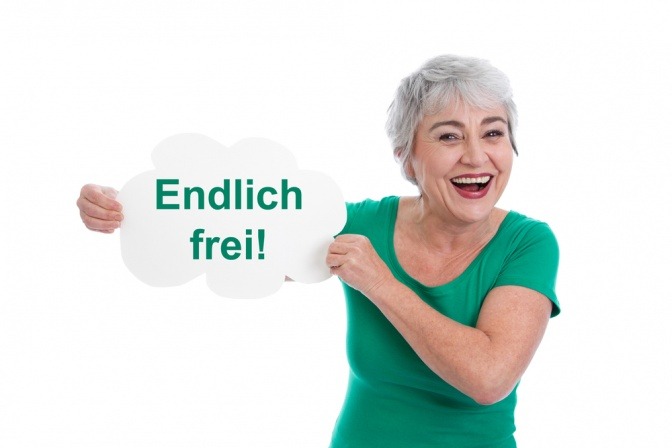 Glückliche Seniorin hält ein Schild mit der Aufschrift "Endlich frei" hoch.