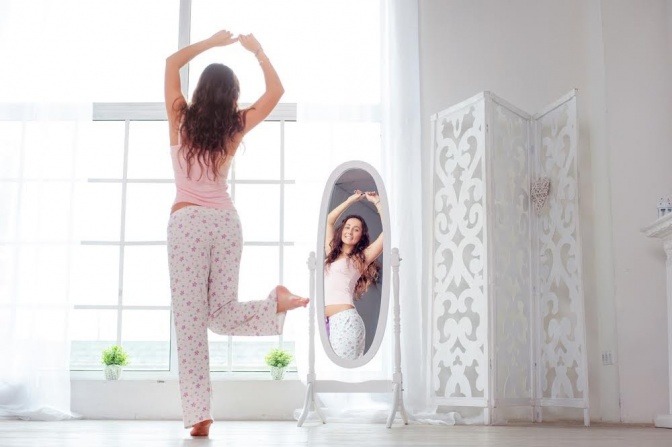 Eine Frau im Pyjama tanzt vor ihrem Spiegel.