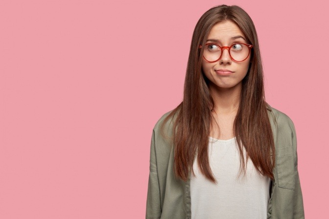 Junge Frau mit Brille wirkt unsicher und blickt fragend nach oben. 